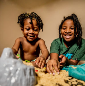Big sister and little brother playing in sand at home during covid19