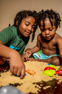 Big sister and little brother playing in sand at home during covid19